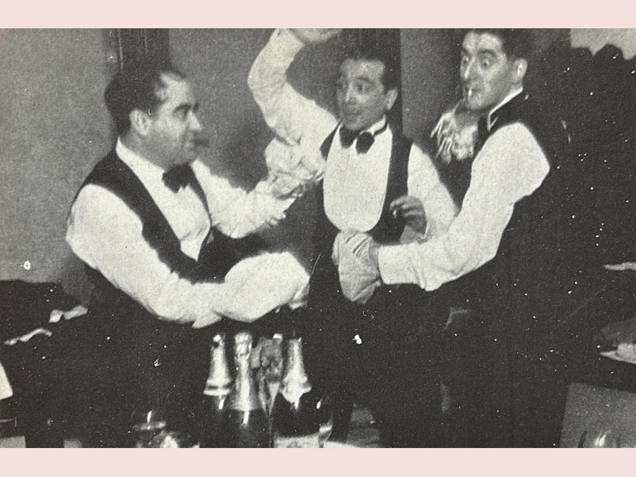 Fig. 7: Imagen sin datar (tal vez mediados de los años 40), en la que, a los postres de un banquete, el locutor radiofónico Bobby Deglané (en el centro) ejerce como árbitro de un combate de boxeo entre el autor Adolfo Torrado (izquierda) y Alfredo Marqueríe. Cabe señalar que este realizó duras críticas de las comedias de su amistoso rival de la foto.